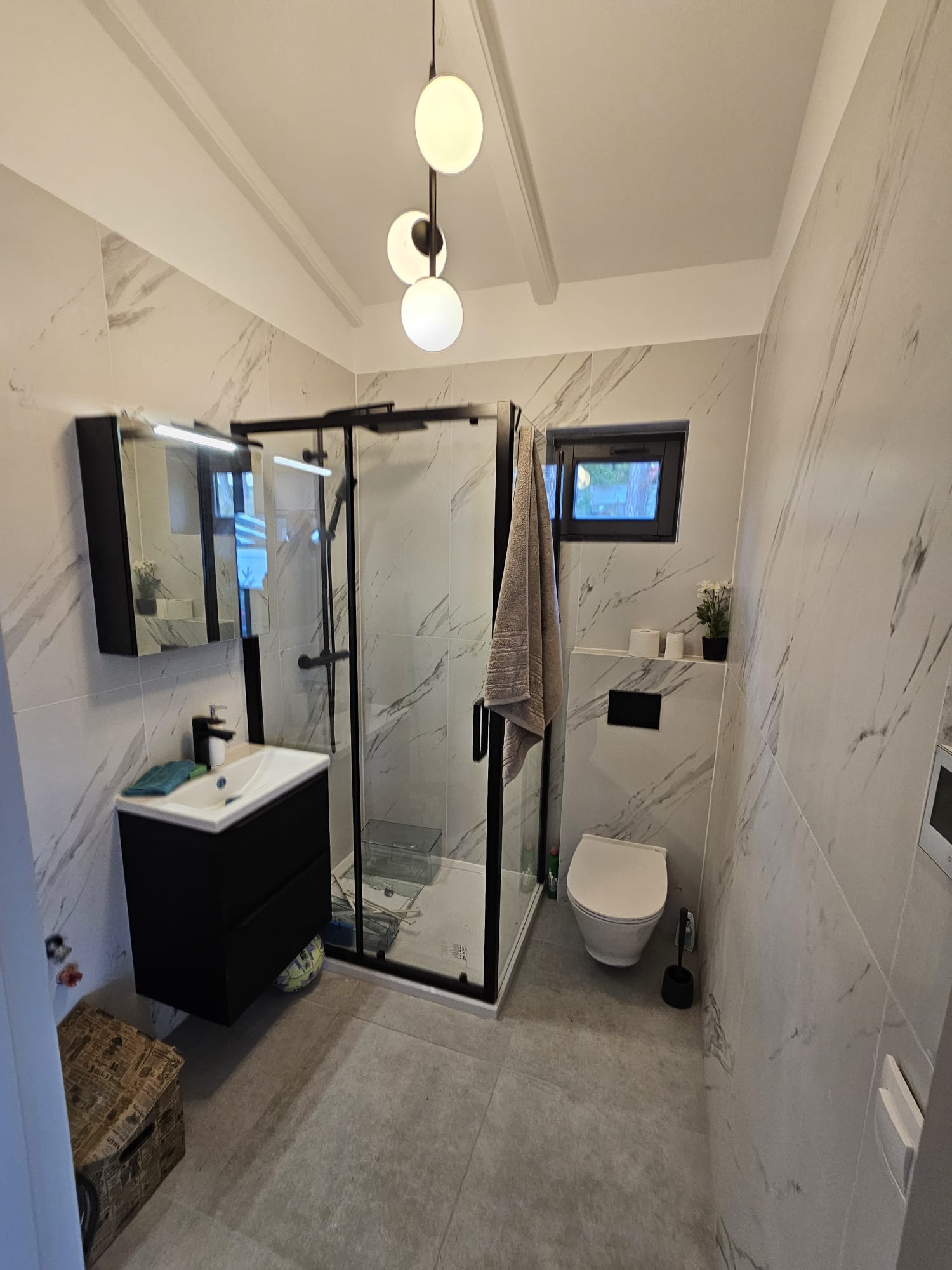A modern bathroom with a white and gray color scheme, featuring a glass-enclosed shower, toilet, and sink.