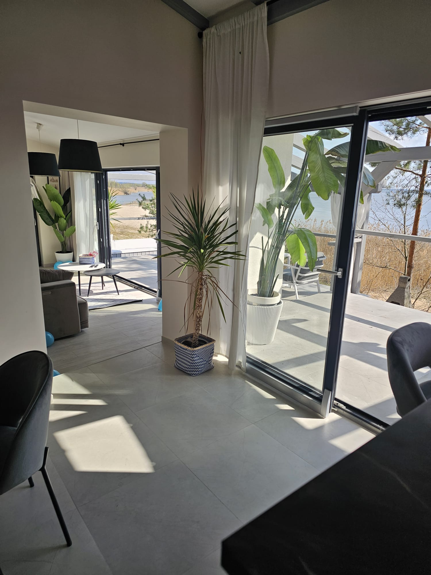 Bright living room at Turawa Beach House with large sofa, coffee table and wide glazing opening to the terrace with lake view, in soft beige and blue tones.