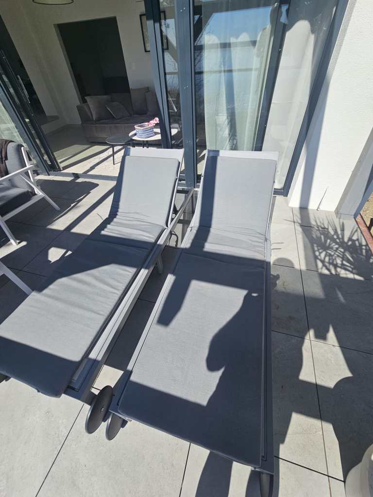 The image depicts a serene outdoor setting, featuring two lounge chairs situated on a patio. The lounge chairs, positioned...